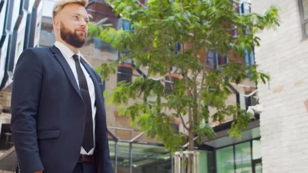 Un hombre de negocios seguro y su colega frente al moderno edificio de oficinas. Los inversores financieros están hablando al aire libre. Banca y negocios. — Vídeos de Stock