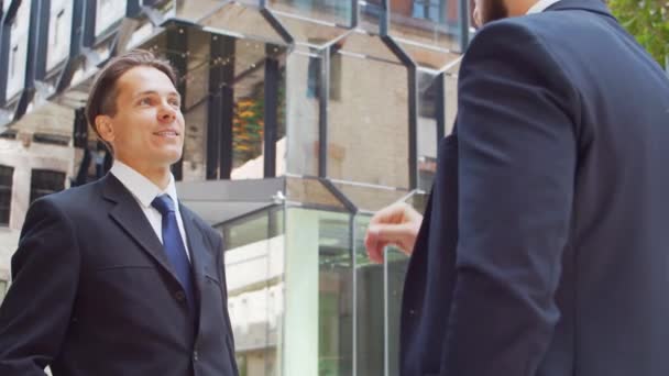 Důvěryhodný podnikatel a jeho kolega před moderní kancelářskou budovou. Finanční investoři mluví venku. Bankovnictví a obchod. — Stock video