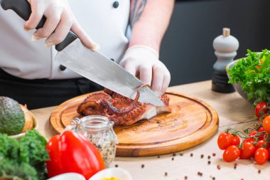 Genç aşçı modern bir mutfakta ahtapot kesiyor. Adam evde yemek hazırlıyor. Sağlıklı ve lezzetli yemekler pişirmek..