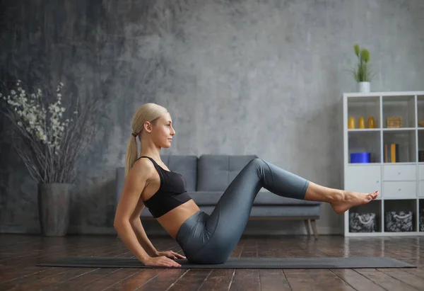 Menina jovem e desportiva em sportswear está fazendo exercícios em casa interior. Fit e mulher loira esbelta entra para esportes e fitness. Saúde, queima de gordura e bem-estar. — Fotografia de Stock