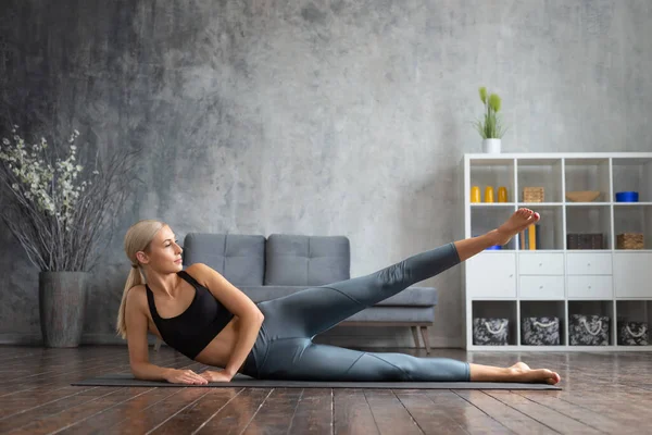 Menina jovem e desportiva em sportswear está fazendo exercícios em casa interior. Fit e mulher loira esbelta entra para esportes e fitness. Saúde, queima de gordura e bem-estar. — Fotografia de Stock