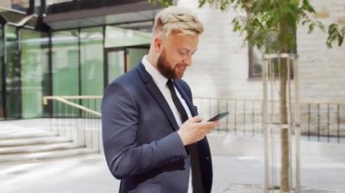 Modern ofis binasının önünde kendinden emin bir iş adamı. Finansal yatırımcı açık havada akıllı telefon kullanıyor. Bankacılık ve iş.
