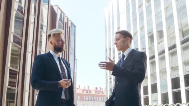 Un hombre de negocios seguro y su colega frente al moderno edificio de oficinas. Los inversores financieros están hablando al aire libre. Banca y negocios. — Vídeos de Stock