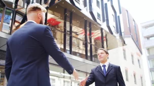 Un hombre de negocios seguro y su colega frente al moderno edificio de oficinas. Los inversores financieros están hablando al aire libre. Banca y negocios. — Vídeo de stock