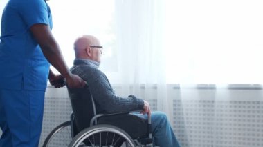 Afro-Amerikalı bakıcı ve tekerlekli sandalyedeki yaşlı engelli adam. Bakımevindeki profesyonel hemşire ve özürlü hasta. Yardım, rehabilitasyon ve sağlık hizmetleri.