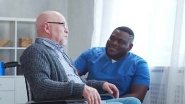 Afro-Amerikalı bakıcı ve tekerlekli sandalyedeki yaşlı engelli adam. Bakımevindeki profesyonel hemşire ve özürlü hasta. Yardım, rehabilitasyon ve sağlık hizmetleri.
