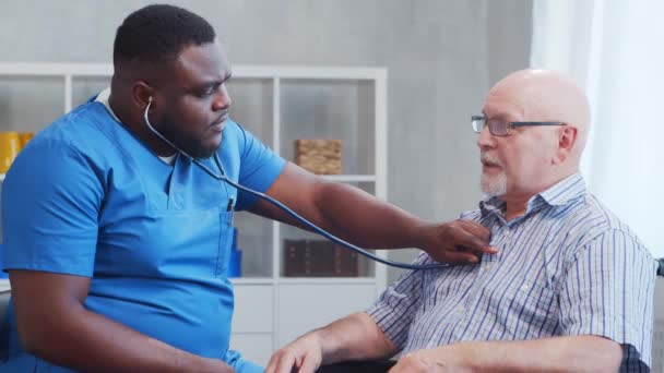 Afro-Amerikaanse verzorger en oude gehandicapte man in een rolstoel. Professionele verpleegkundige en gehandicapte patiënt in een verpleeghuis. Bijstand, rehabilitatie en gezondheidszorg. — Stockvideo
