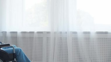 Engelli yaşlı adam evde tek başına tekerlekli sandalyede oturuyor. Tekerlekli sandalyedeki engelli pencereden dışarı bakıyor. Felç ve sakatlık.