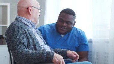 Afro-Amerikalı bakıcı ve tekerlekli sandalyedeki yaşlı engelli adam. Bakımevindeki profesyonel hemşire ve özürlü hasta. Yardım, rehabilitasyon ve sağlık hizmetleri.