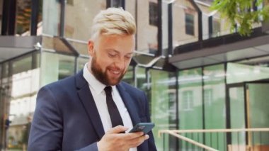 Modern ofis binasının önünde kendinden emin bir iş adamı. Finansal yatırımcı açık havada akıllı telefon kullanıyor. Bankacılık ve iş.