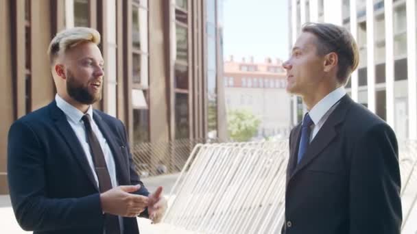 Un hombre de negocios seguro y su colega frente al moderno edificio de oficinas. Los inversores financieros están hablando al aire libre. Banca y negocios. — Vídeos de Stock