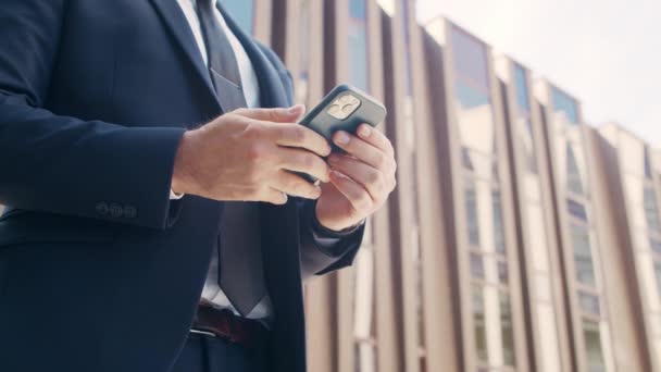 Empresário confiante em frente ao edifício de escritórios moderno. investidor financeiro está usando smartphone ao ar livre. Banca e negócios. — Vídeo de Stock