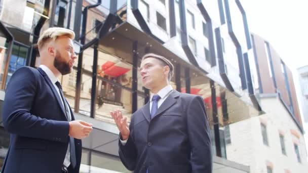 Homme d'affaires confiant et son collègue devant un immeuble de bureaux moderne. Les investisseurs financiers parlent en plein air. Banques et entreprises. — Video