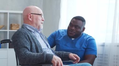 Afro-Amerikalı bakıcı ve tekerlekli sandalyedeki yaşlı engelli adam. Bakımevindeki profesyonel hemşire ve özürlü hasta. Yardım, rehabilitasyon ve sağlık hizmetleri.