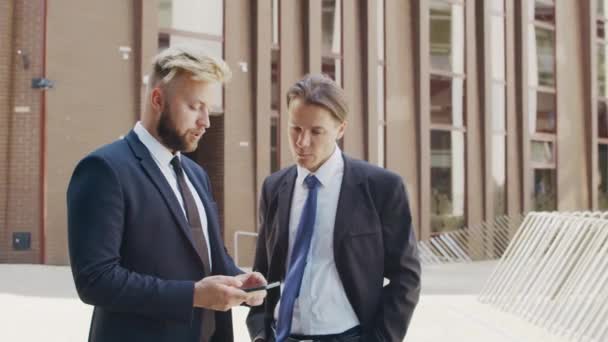 Pewny siebie biznesmen i jego kolega przed nowoczesnym budynkiem biurowym. Inwestorzy finansowi rozmawiają na zewnątrz. Bankowość i biznes. — Wideo stockowe