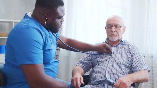 Afro-Amerikaanse verzorger en oude gehandicapte man in een rolstoel. Professionele verpleegkundige en gehandicapte patiënt in een verpleeghuis. Bijstand, rehabilitatie en gezondheidszorg. — Stockvideo