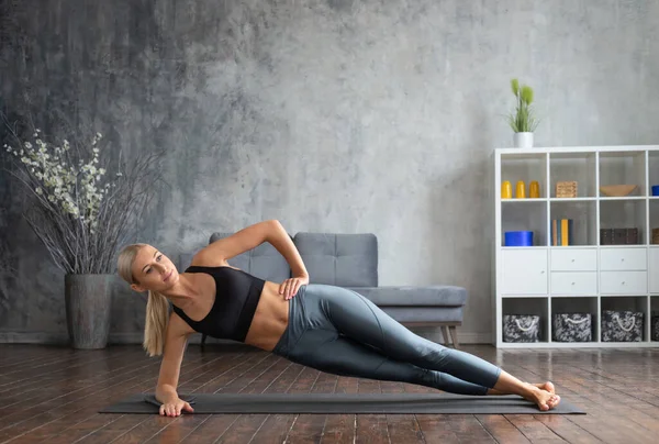 Menina jovem e desportiva em sportswear está fazendo exercícios em casa interior. Fit e mulher loira esbelta entra para esportes e fitness. Saúde, queima de gordura e bem-estar. — Fotografia de Stock