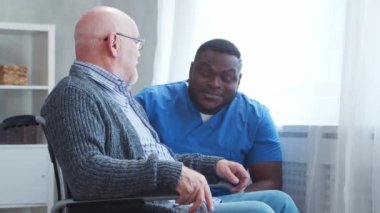 Afro-Amerikalı bakıcı ve tekerlekli sandalyedeki yaşlı engelli adam. Bakımevindeki profesyonel hemşire ve özürlü hasta. Yardım, rehabilitasyon ve sağlık hizmetleri.