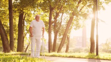 Engelli yaşlı adam bir yürüteçle yürüyor. Parktaki özürlü hasta. Yardım, rehabilitasyon ve sağlık hizmetleri. Altın saat gün batımı.