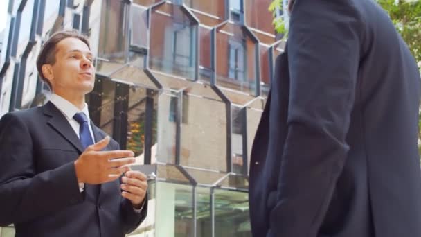 Un hombre de negocios seguro y su colega frente al moderno edificio de oficinas. Los inversores financieros están hablando al aire libre. Banca y negocios. — Vídeos de Stock