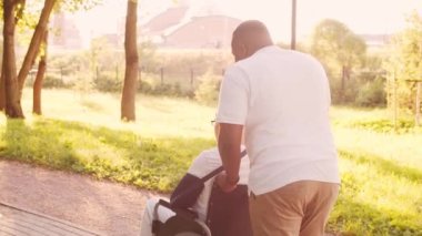 Afro-Amerikalı bakıcı ve tekerlekli sandalyedeki yaşlı engelli adam. Parktaki profesyonel hemşire ve özürlü hasta. Yardım, rehabilitasyon ve sağlık hizmetleri. Altın saat gün batımı.