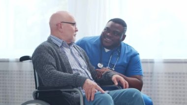 Afro-Amerikalı bakıcı ve tekerlekli sandalyedeki yaşlı engelli adam. Bakımevindeki profesyonel hemşire ve özürlü hasta. Yardım, rehabilitasyon ve sağlık hizmetleri.