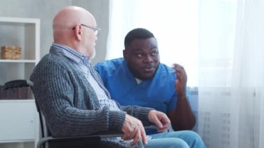 Afro-Amerikalı bakıcı ve tekerlekli sandalyedeki yaşlı engelli adam. Bakımevindeki profesyonel hemşire ve özürlü hasta. Yardım, rehabilitasyon ve sağlık hizmetleri.