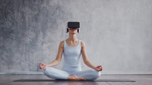 Chica joven y deportiva en ropa deportiva está haciendo ejercicios de yoga utilizando casco de realidad virtual. Ajuste y delgada mujer rubia entra en los deportes y la aptitud. Salud, quemaduras de grasa y. — Vídeos de Stock