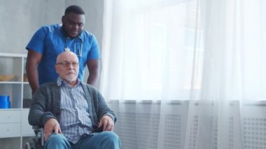 Afro-Amerikalı bakıcı ve tekerlekli sandalyedeki yaşlı engelli adam. Bakımevindeki profesyonel hemşire ve özürlü hasta. Yardım, rehabilitasyon ve sağlık hizmetleri.