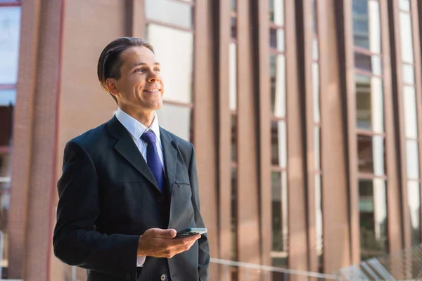 Un hombre de negocios seguro frente al moderno edificio de oficinas. El inversor financiero está utilizando teléfono inteligente al aire libre. Banca y negocios. — Foto de Stock