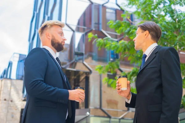 Un hombre de negocios seguro y su colega frente al moderno edificio de oficinas. Los inversores financieros están hablando al aire libre. Banca y negocios. — Foto de Stock