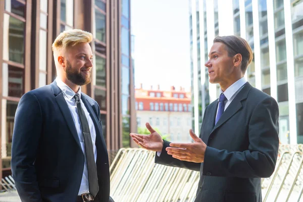 Selbstbewusster Geschäftsmann und sein Kollege vor einem modernen Bürogebäude. Finanzinvestoren reden im Freien. Banken und Unternehmen. — Stockfoto