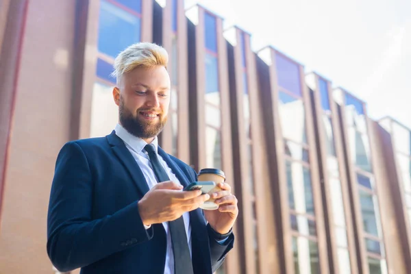 Selbstbewusster Geschäftsmann vor einem modernen Bürogebäude. Finanzinvestor setzt auf Smartphone-Outdoor Banken und Unternehmen. — Stockfoto