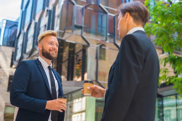 Selbstbewusster Geschäftsmann und sein Kollege vor einem modernen Bürogebäude. Finanzinvestoren reden im Freien. Banken und Unternehmen. — Stockfoto
