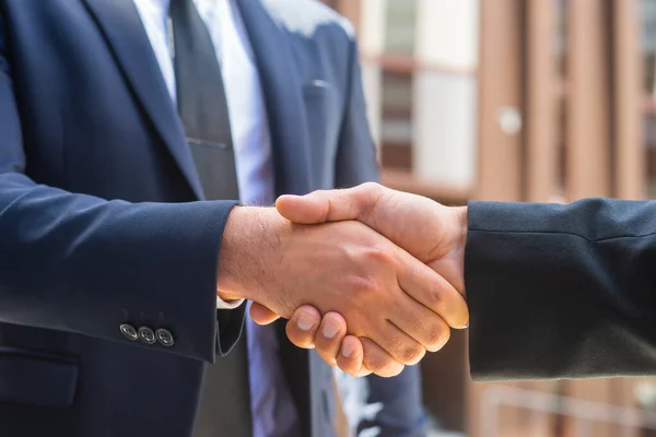 Stringi la mano. L'uomo d'affari e il suo collega si stanno stringendo la mano davanti a un moderno edificio per uffici. Investitori finanziari all'aperto. Settore bancario e commerciale. — Foto Stock