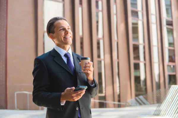 Selbstbewusster Geschäftsmann vor einem modernen Bürogebäude. Finanzinvestor setzt auf Smartphone-Outdoor Banken und Unternehmen. — Stockfoto