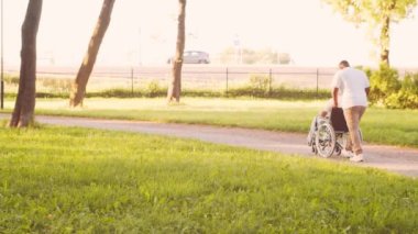 Afro-Amerikalı bakıcı ve tekerlekli sandalyedeki yaşlı engelli adam. Parktaki profesyonel hemşire ve özürlü hasta. Yardım, rehabilitasyon ve sağlık hizmetleri. Altın saat gün batımı.