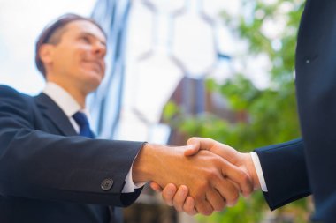 El sıkışın, yakın plan. İş adamı ve meslektaşı modern ofis binasının önünde el sıkışıyorlar. Finansal yatırımcılar açık havada. Bankacılık ve iş.
