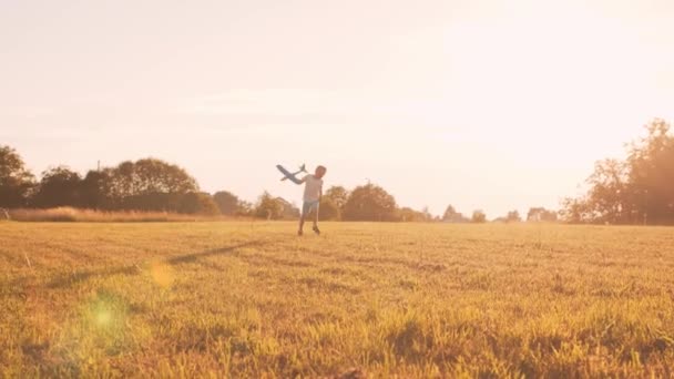 El chico juega con un avión de juguete en un campo al atardecer. El concepto de infancia, libertad e inspiración. — Vídeo de stock