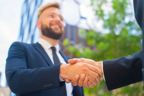 Handshake close-up. Businessman and his colleague are shaking hands in front of modern office building. Financial investors outdoor. Banking and business.