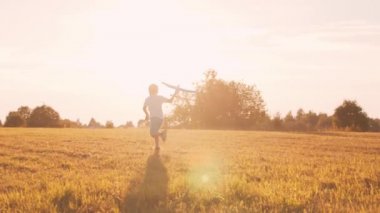 Çocuk gün batımında bir tarlada oyuncak bir uçakla oynuyor. Çocukluk, özgürlük ve ilham konsepti.