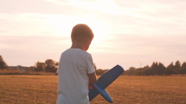 A fiú egy játékgéppel játszik egy mezőn naplementekor. A gyermekkor, a szabadság és az inspiráció fogalma. — Stock videók