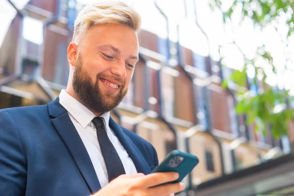 Fiducioso uomo d'affari di fronte a un moderno edificio per uffici. Investitore finanziario utilizza smartphone all'aperto. Settore bancario e commerciale. — Foto Stock