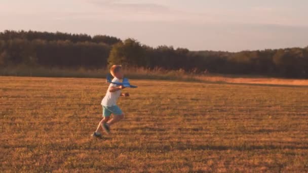 Jongen speelt met een speelgoedvliegtuig in een veld bij zonsondergang. Het concept van kindertijd, vrijheid en inspiratie. — Stockvideo