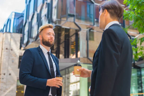 Zelfverzekerde zakenman en zijn collega tegenover modern kantoorgebouw. Financiële investeerders hebben het over buitenshuis. Bankieren en bedrijfsleven. — Stockfoto