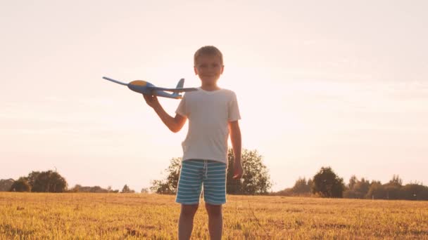 Хлопчик грає з іграшковим літаком на полі на заході сонця. Поняття дитинства, свободи та натхнення . — стокове відео