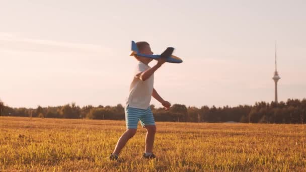 Jongen speelt met een speelgoedvliegtuig in een veld bij zonsondergang. Het concept van kindertijd, vrijheid en inspiratie. — Stockvideo