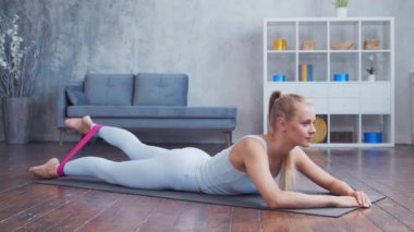 Spor giyim sektöründe genç ve sportif bir kız iç mekanda egzersiz yaparken direniş bandı kullanıyor. Formda ve narin sarışın kadın spor ve spor için geliyor. Sağlık sigortası, yağ yakma ve sağlık..