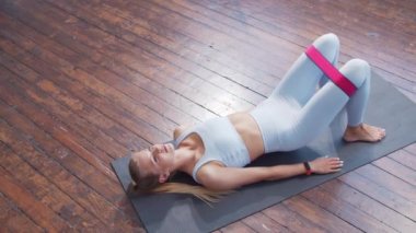 Spor giyim sektöründe genç ve sportif bir kız iç mekanda egzersiz yaparken direniş bandı kullanıyor. Formda ve narin sarışın kadın spor ve spor için geliyor. Sağlık sigortası, yağ yakma ve sağlık..
