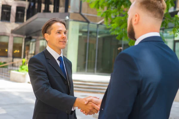 有信心的商人和他的同事正在现代办公大楼前握手。金融投资者在户外。银行和商业. — 图库照片